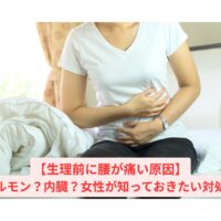 生理前に腰が痛い女性がベッドに座りながらお腹を押さえている様子